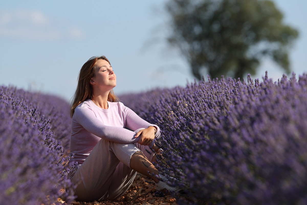Woman sitting in field of lavender with eyes closed looking peaceful, after doing EFT Tapping for anxiety