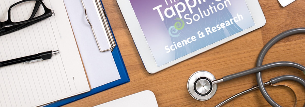 Desktop filled with paperwork, pen, glasses, stethoscope, and booklet on The Tapping Solution Science and Research